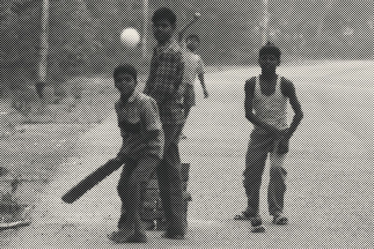 Halftone photograph: boys playing street cricket on a road in Agra, the ball in the air.